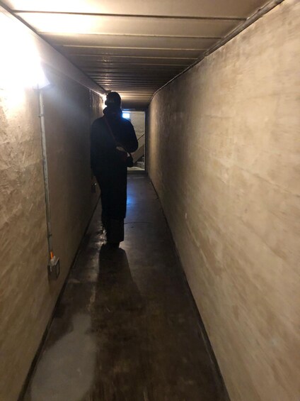 A person walking down a dimly lit, narrow corridor with concrete walls and a metal ceiling. 1