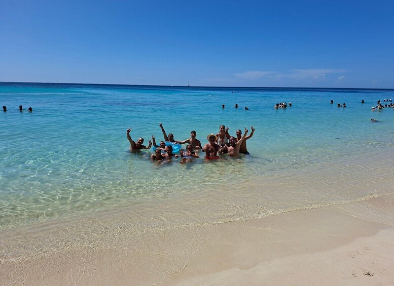 A group of people in shallow water on a beach, with clear skies and calm sea. 1