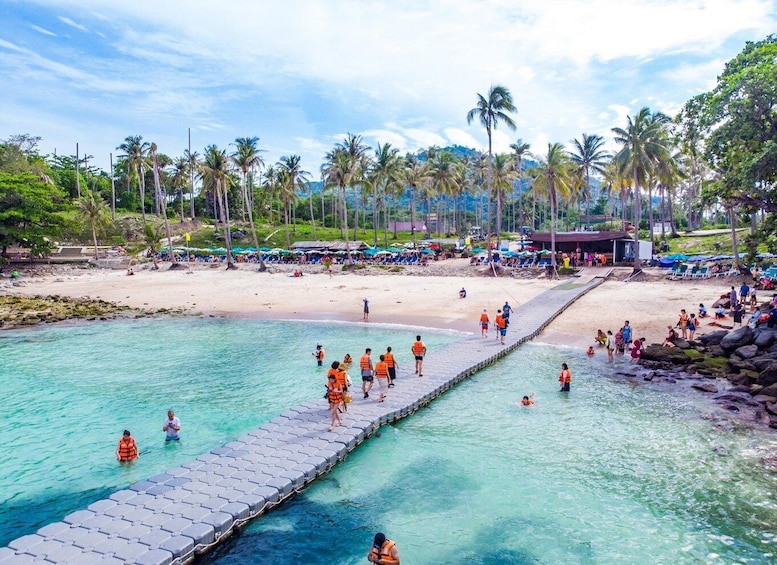 A beach with clear turquoise water, a wooden walkway, and palm trees. 4