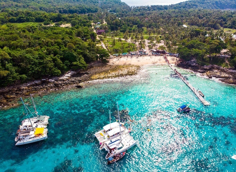 A coastal area with clear turquoise waters, boats docked, and a beach with people. 3