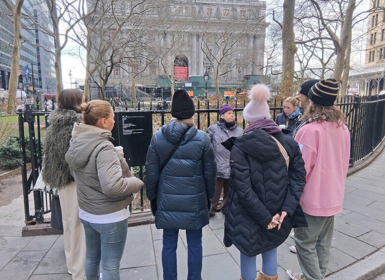 A group of people standing on a sidewalk, facing a large building with a sign. 5