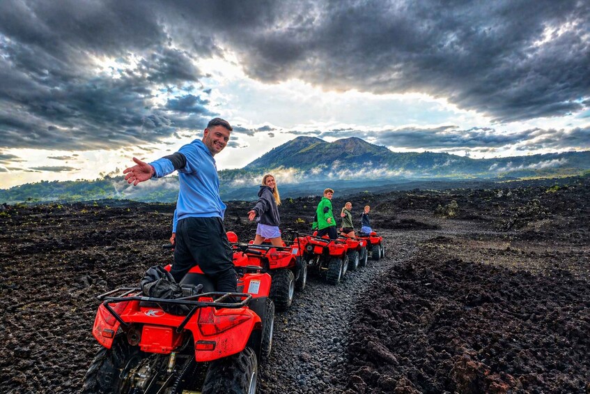 People riding red ATVs on a lava field with a mountain in the background. 1