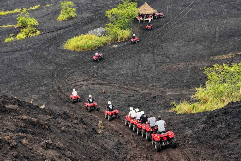 A group of people riding red ATVs on a dirt track with a thatched-roof structure in the background. 2