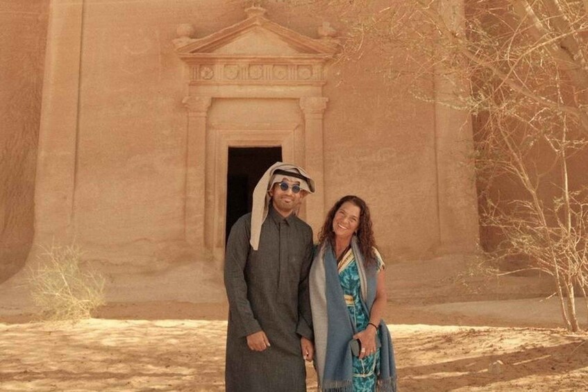 A man and a woman standing in front of a large ancient building with a doorway. 4
