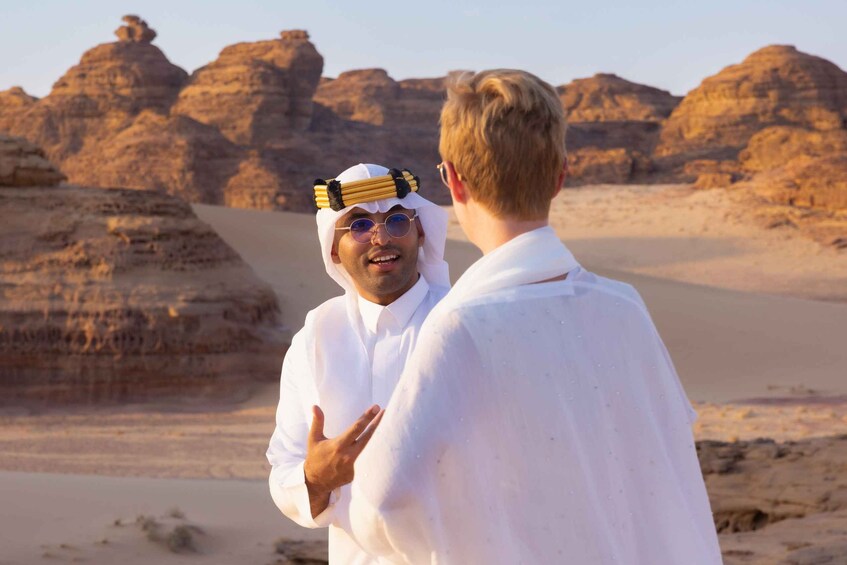 Two individuals in a desert landscape with rocky formations and sand dunes. 3