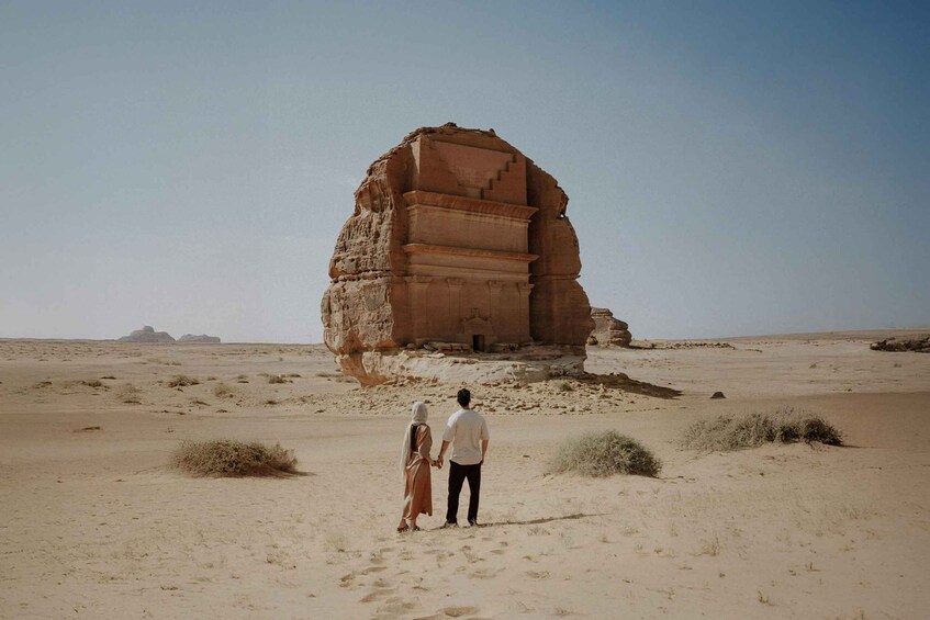 A couple standing in a desert with a large rock formation in the background. 1