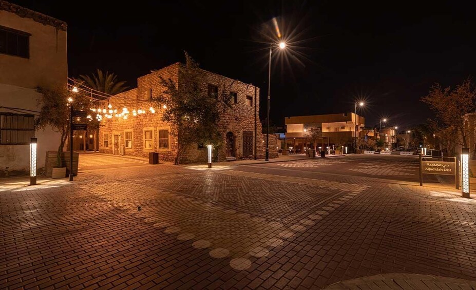 A nighttime street scene with stone buildings, street lamps, and a sign indicating Aljazeera District. 2