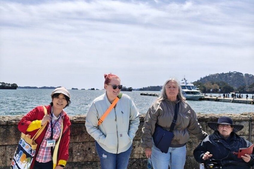 A group of people standing by a waterfront with a boat in the background. 2