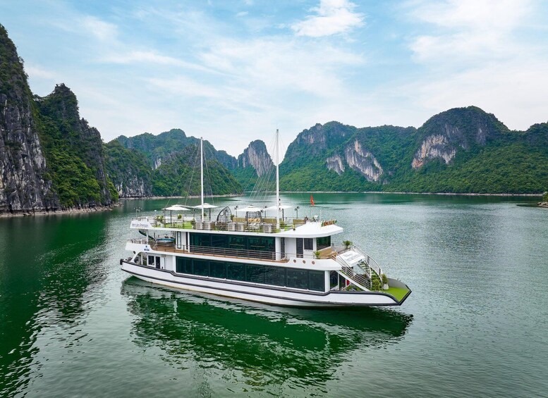 A white river cruise boat with a deck and a flag, surrounded by green cliffs and calm water. 2
