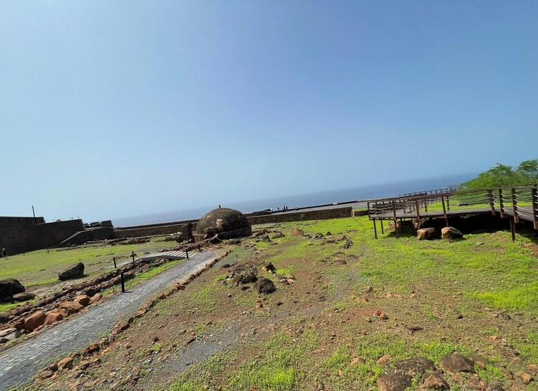 Una fortificación costera con una gran estructura en forma de cúpula, un paseo pavimentado y una plataforma de madera con vistas al mar. 4