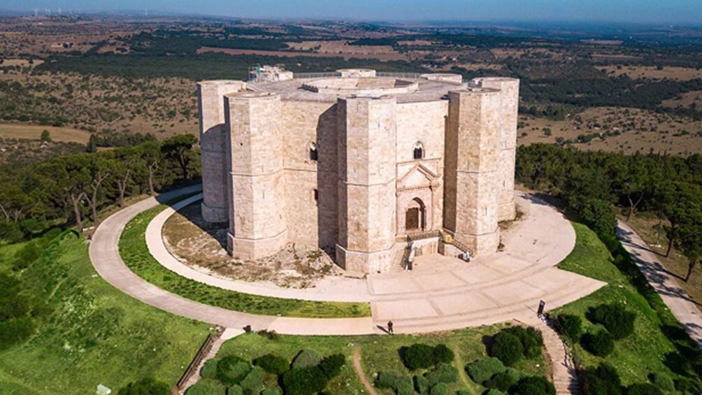 A large, circular stone structure with a central entrance, surrounded by a landscaped area with trees and a clear sky. 2