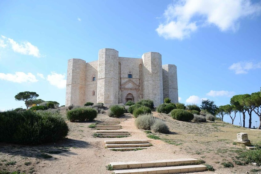 A historic stone castle with a central entrance, surrounded by a well-maintained garden and a clear sky. 1