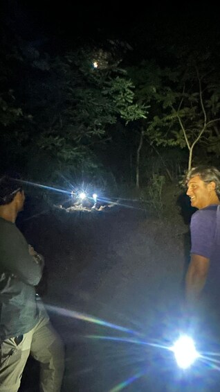 Two people with flashlights in a dark outdoor setting, possibly a forest or wooded area. 4