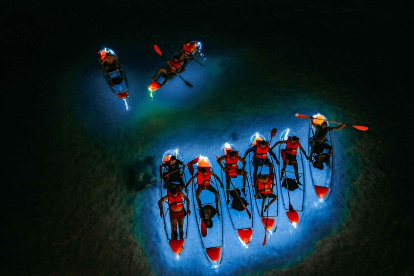 A group of kayakers in a circular formation on a body of water at night. 1