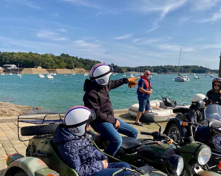 People on motorcycles and a boat near a body of water with boats in the background. 3