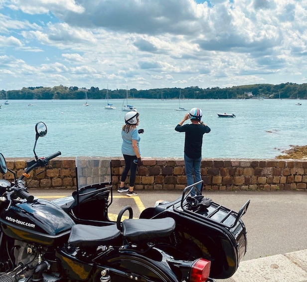 A coastal scene with a stone wall, a parked motorcycle, and a person taking a photo. 2