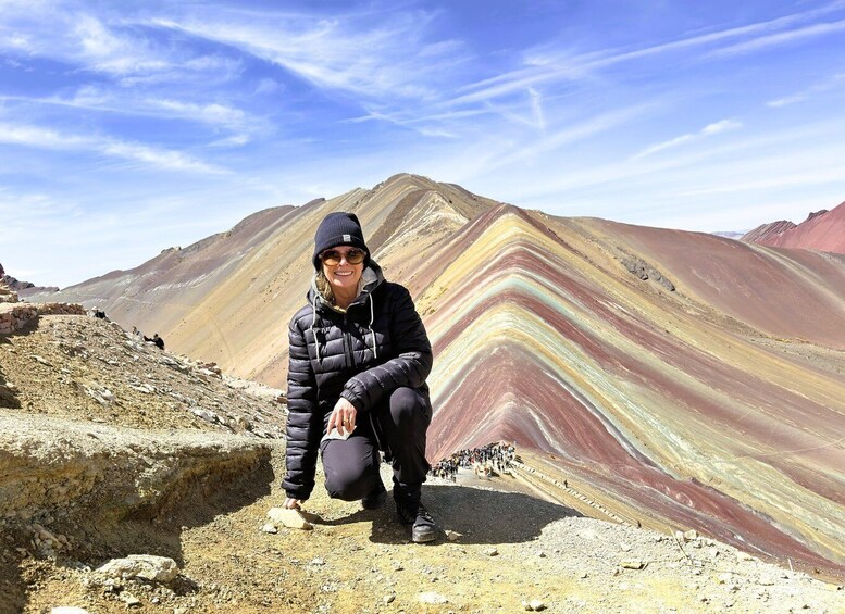 En person hukar på en klippavsats med en färgstark geologisk formation i bakgrunden. 3