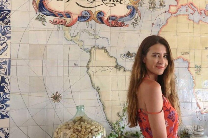 A person standing in front of a decorative map with a bottle of snacks and a glass of water on a table. 4