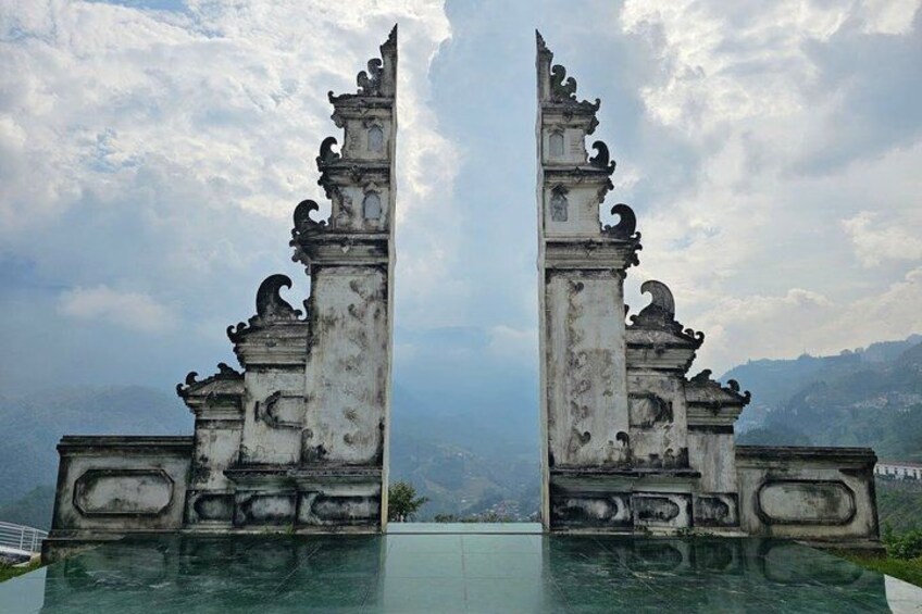 A symmetrical stone structure with ornate carvings, set against a cloudy sky and a mountainous backdrop. 3