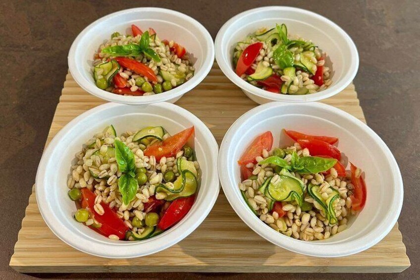 Four white bowls containing a salad with rice, peas, cucumbers, and tomatoes on a wooden board. 5