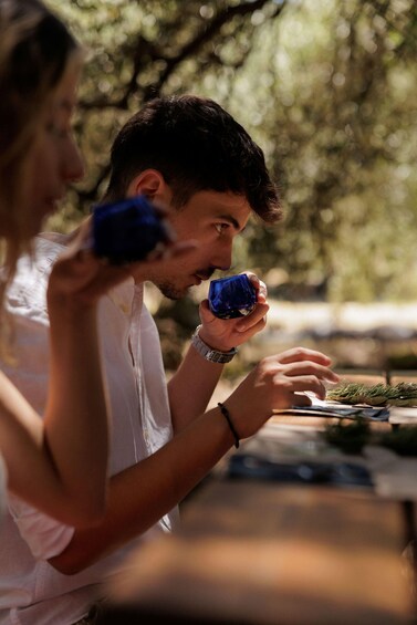 A person holding a blue object, possibly a drink, with a blurred background of greenery. 5