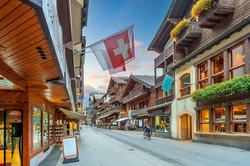 A street with wooden buildings, a cyclist, and a Swiss flag. 4