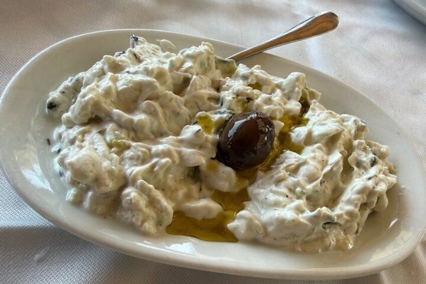 A white plate with a creamy dish, possibly a dip or spread, with a spoon and a single olive on top. 2