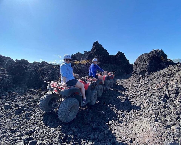 Two people on ATVs on rocky terrain with volcanic rock formations in the background. 2