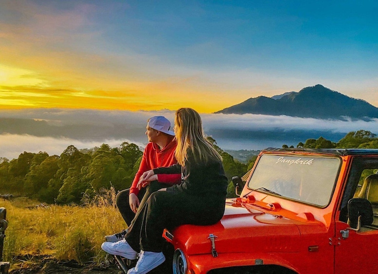 Two people sitting on a red vehicle with a mountainous landscape and a sunset in the background. 4