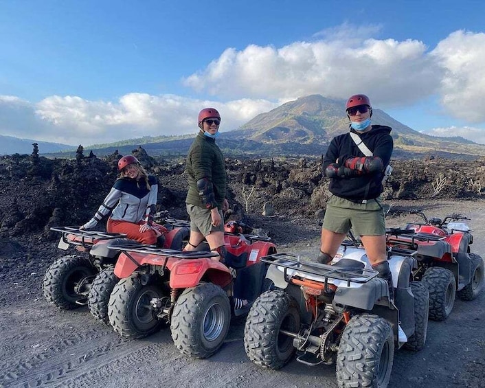Three people on ATVs in a volcanic landscape with a mountain in the background. 5