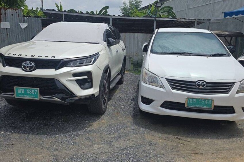 Two white Toyota Fortuner cars parked on a gravel surface with a corrugated metal roof and a blue tarp in the background. 2