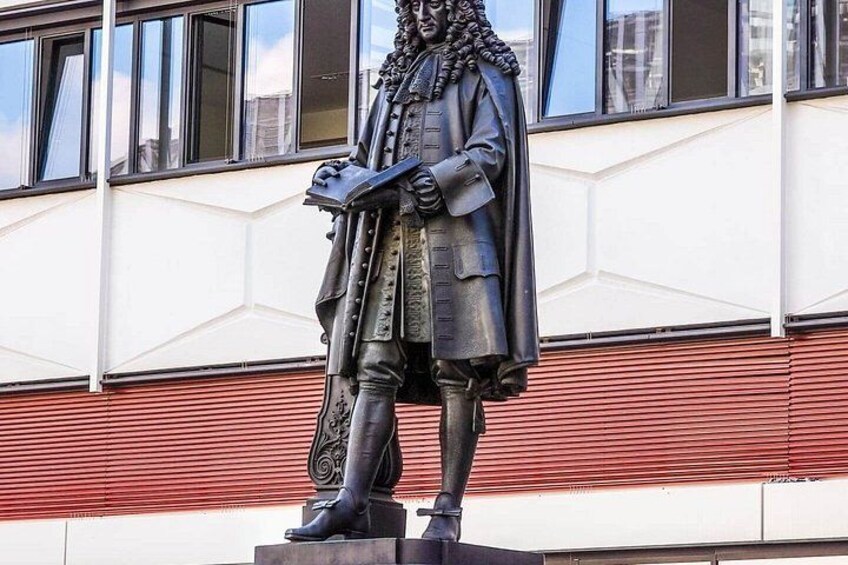 A statue of a historical figure in period clothing, standing on a pedestal, with a building in the background. 5