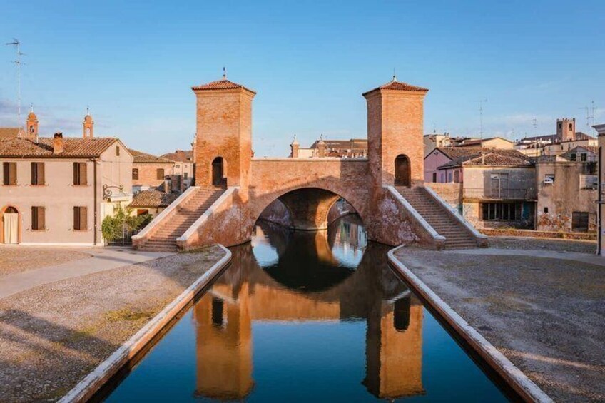 A stone bridge over a canal with buildings on either side. 5