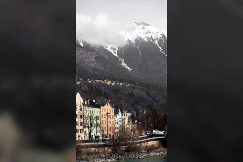 A mountain range with snow-capped peaks, a town with colorful buildings, and a river with a bridge. 2