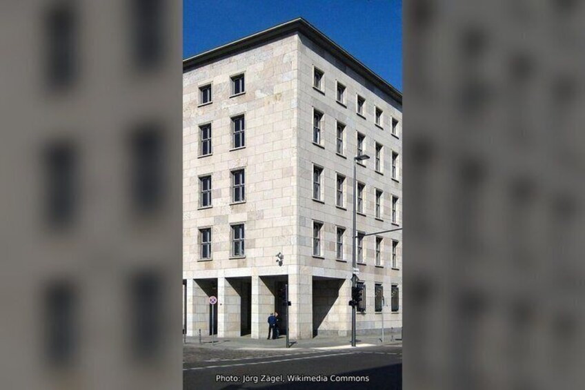 A multi-story building with a stone facade, a pedestrian crossing, and a traffic light. 5