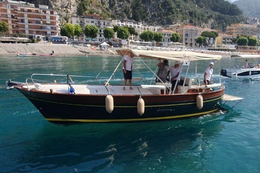A wooden boat with people on it, floating on water with a coastal town in the background. 2