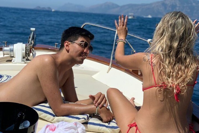 Two people on a boat, one wearing a red bikini and the other in swimwear, with a clear view of the sea and distant mountains. 4
