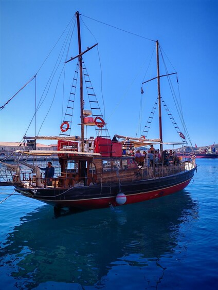 A traditional sailing boat docked at a harbor with passengers on board. 5