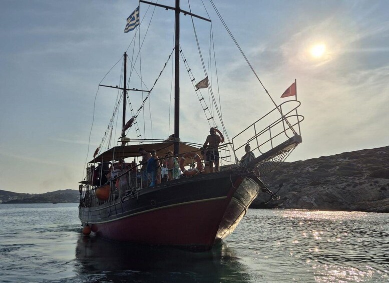 A boat with people on board, anchored near a rocky shoreline with the sun setting in the background. 1
