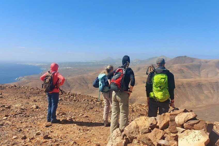 Four hikers on a rocky mountain trail with a view of the ocean and distant hills. 4