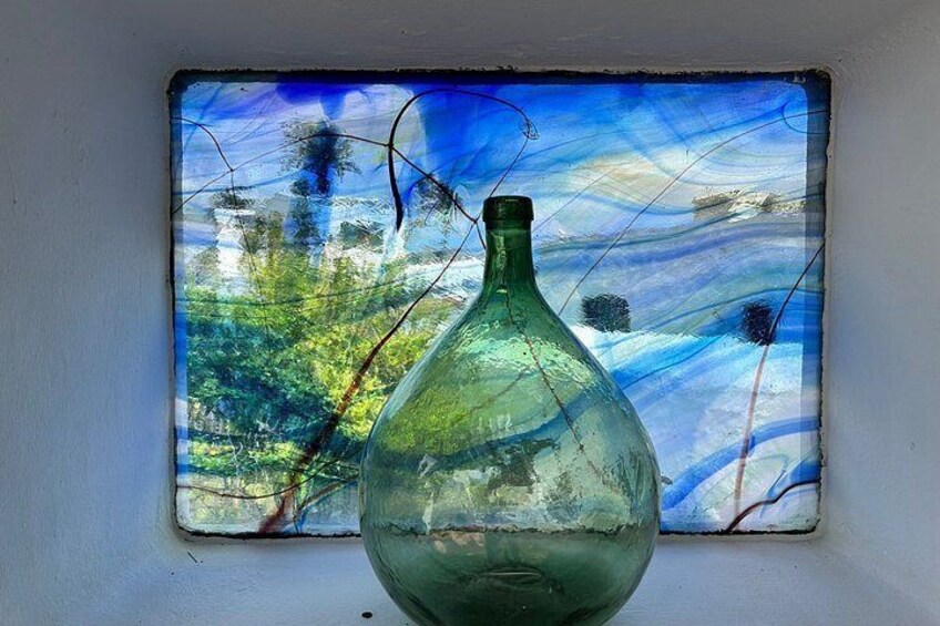 A green glass vase on a windowsill with a colorful abstract painting in the background. 5