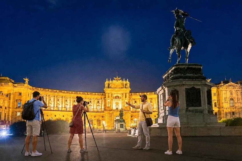 A nighttime scene with a statue, a large illuminated building, and people taking photos. 3