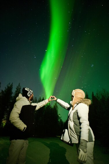 Two people making a heart shape with their hands under the Northern Lights. 1