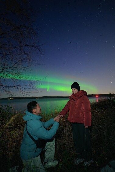 Two people holding hands by a lake at night with the aurora borealis in the sky. 2