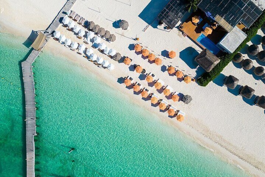 A beach with rows of umbrellas and lounge chairs, a pier extending into the water, and a building with a blue roof. 1