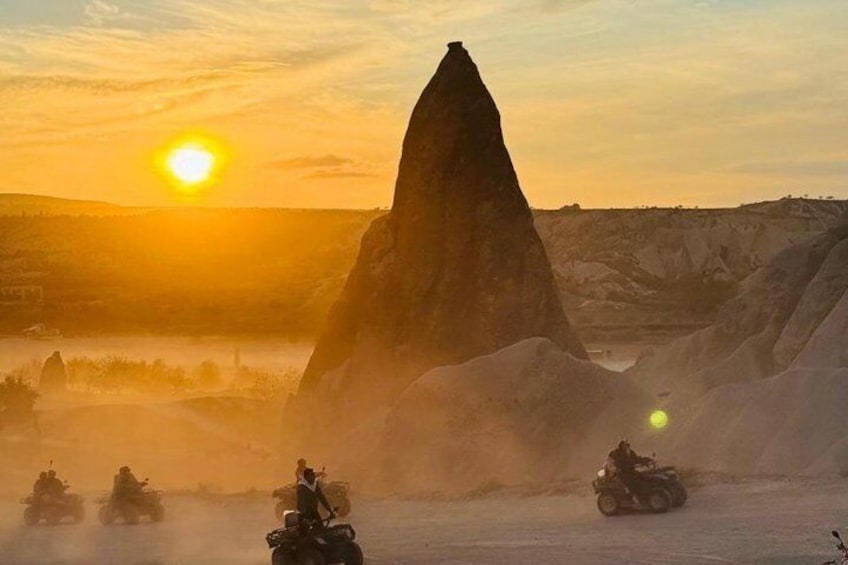 A sunset over a rocky landscape with a prominent peak and riders on off-road vehicles. 4