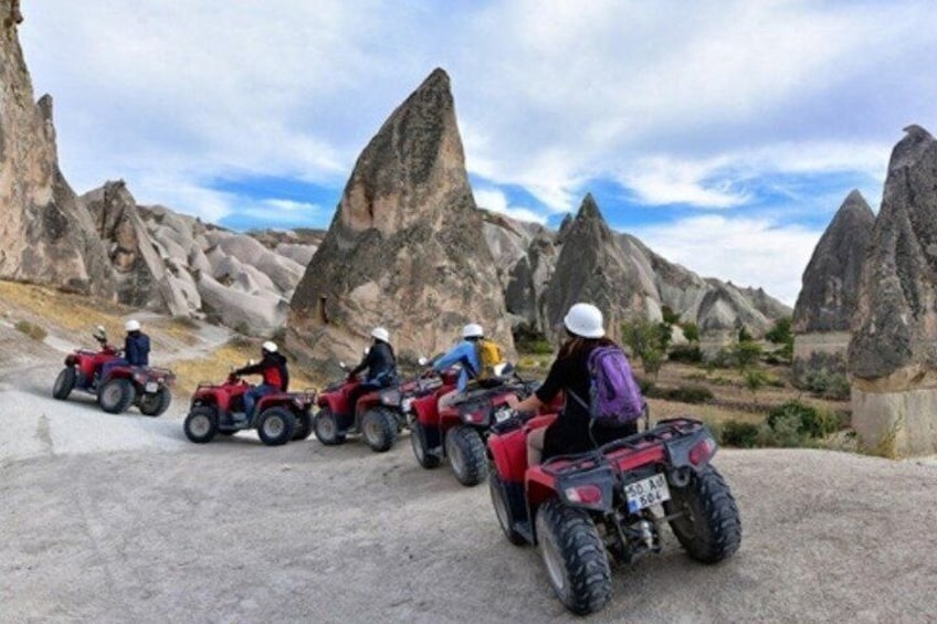 A group of people riding ATVs on a rocky terrain with large rock formations in the background. 1