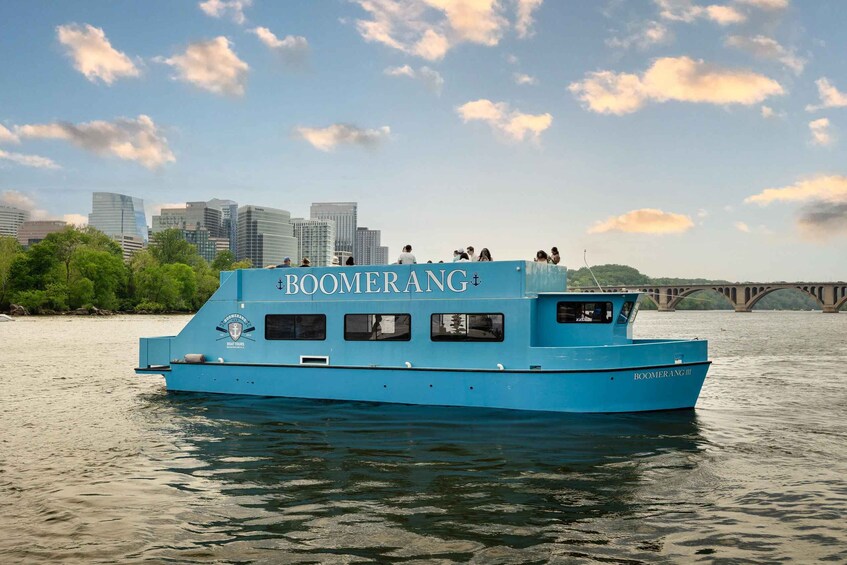 A blue boat named BOOMERANG III on calm water with a city skyline and a bridge in the background. 3