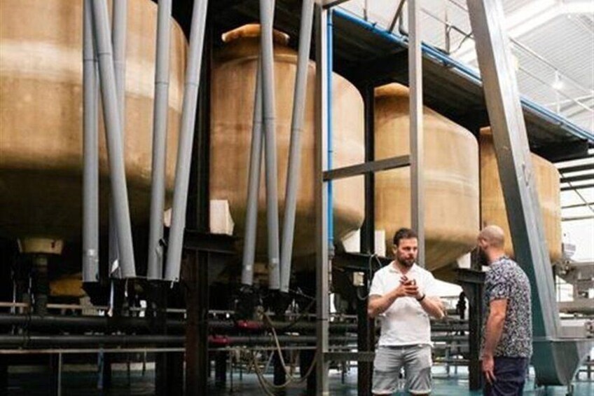 Two people standing in a facility with large cylindrical tanks and pipes. 2