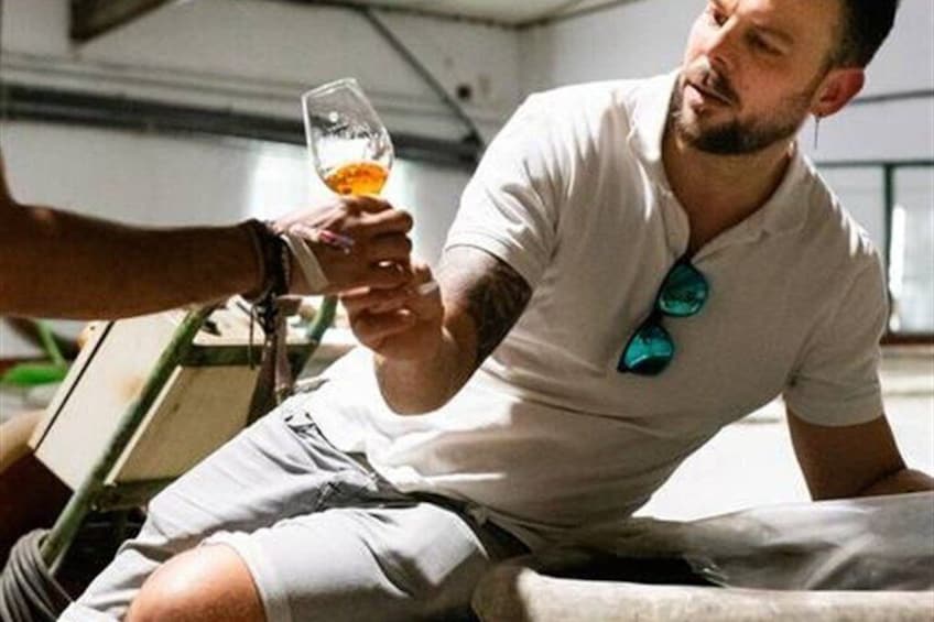 A person sitting on a boat, holding a glass of amber liquid, with sunglasses hanging from their shirt. 3